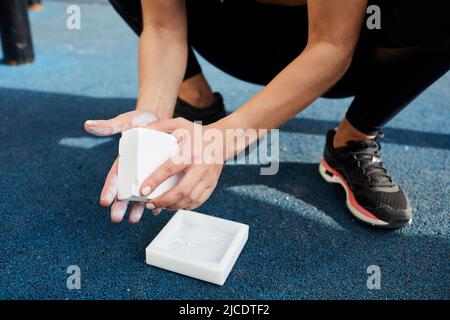 Primo piano di una donna irriconoscibile che si accovacciano e che usa gymnastic galk per spargere sulle mani prima dell'esercitazione del peso Foto Stock