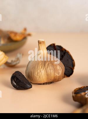 Bulbi d'aglio nero, spicchi e buccia giacciono su un tavolo beige. Una composizione concettuale di aglio nero fermentato. Alimentazione sana, cibo vegetariano Foto Stock