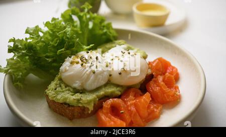 Lo chef cosparge i semi di pane tostato con uova in camicia e guacamole. Delizioso toast servito con fette di trota e insalata fresca lascia il closeup estremo Foto Stock