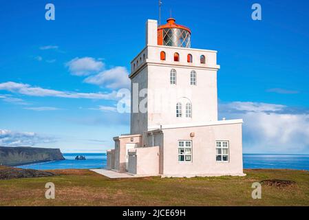 Bellissimo faro di Dyrholaey sulla scogliera a Reynisfjara mare contro il cielo blu Foto Stock