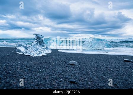 Iceberg si sbanda sulla spiaggia di sabbia nera con onde che precipitano a riva contro il cielo Foto Stock