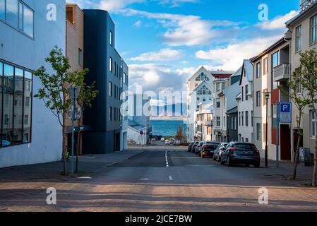 Auto parcheggiate su strada tra edifici in città che conducono verso il mare contro il cielo Foto Stock