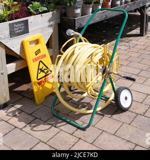 Una bobina per tubi da giardino con tubo resistente al kink giallo su bobine portatili e con ugelli a spruzzo pratica distribuzione in un centro di giardino scentrante Foto Stock