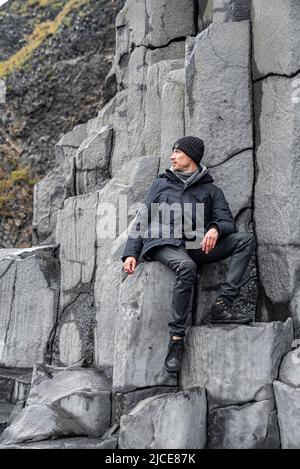 Turista che guarda via mentre si siede su colonne di basalto alla spiaggia di Reynisfjara Foto Stock