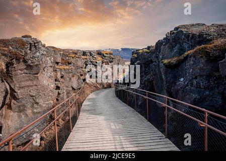 I turisti che camminano sul ponte tra formazioni rocciose nel parco nazionale di Thingvellir Foto Stock