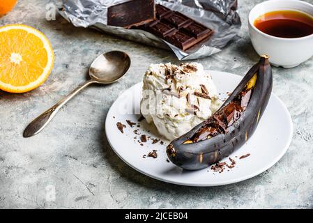 Dolce dessert. Banana alla griglia con cioccolato fondente, succo di agrumi e gelato alla vaniglia. Foto Stock