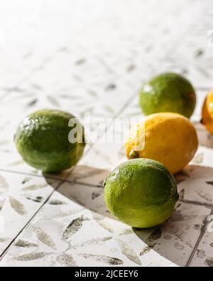 Lime verdi fresche e limoni frutta su piastrelle di ceramica stampate bianche. Spazio di testo Foto Stock