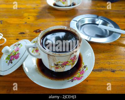 Tazza bianca di caffè caldo su sfondo di legno con posacenere e sigaretta Foto Stock