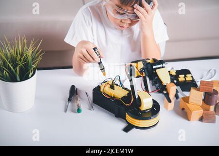 Bambino imparando riparare ottenendo il braccio robot di controllo della lezione, ragazzo piccolo asiatico felice usando il cacciavite per fissare le viti braccio della macchina robotica in casa WO Foto Stock