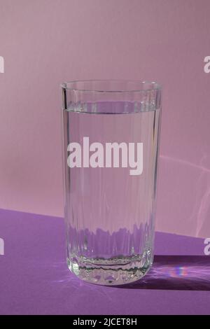 Proiezione ottica, diagonale, isometrica di alta qualità, vita morta di vetro d'acqua su sfondo viola viola. Spazio di copia per il testo. Cocktail liquido bevanda alcolica Foto Stock