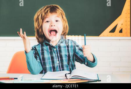 Bambino cordiale in classe vicino alla scrivania da lavagna. I bambini si preparano per la scuola. Felice carino industrious bambino è seduto ad una scrivania all'interno. Foto Stock