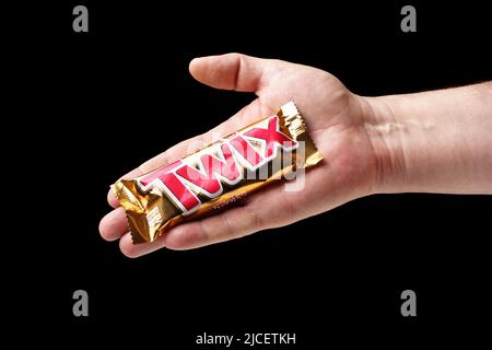 Un uomo offre una barra di cioccolato Twix, mano che tiene una barra di cioccolato primo piano, sfondo nero Foto Stock