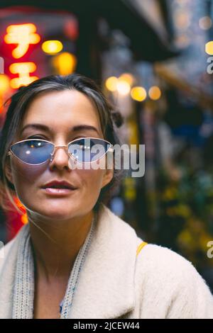 Ritratto di una donna attraente che indossa occhiali blu in un quartiere giapponese. Foto verticale. Foto Stock