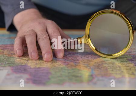 Un uomo tiene una lente d'ingrandimento in mano sopra una mappa. Uomo di mezza età con una lente d'ingrandimento in una cornice d'oro. I nomi sono scritti in ucraino. Foto Stock