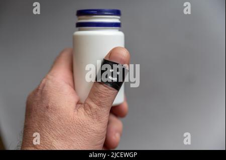 L'uomo di mezza età tiene in mano la medicina bianca o la fiala di vitamina. Phalanx il pollice si avvolse attorno al nastro elettrico nero. Il viso felice e sorridente è dipinto Foto Stock