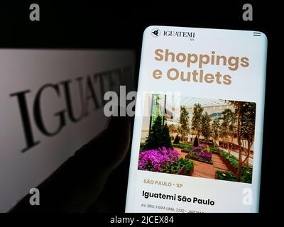 Persona che detiene il cellulare con pagina web della società Iguatemi Empresa de Shopping Centres SA su schermo con logo. Concentrarsi sul centro del display del telefono. Foto Stock