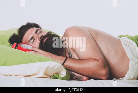 Concetto di allarme. Bell'uomo che dorme a letto. La persona addormentata e pigra si pone lentamente da sola. Ha bisogno di un po' di riposo. Giovane uomo che dorme su cuscini morbidi a letto Foto Stock