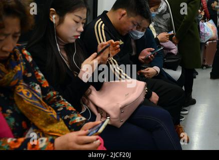 Gli abitanti del luogo utilizzano i loro smartphone sulla pioggia della metropolitana a Nanjing, Cina. Foto Stock