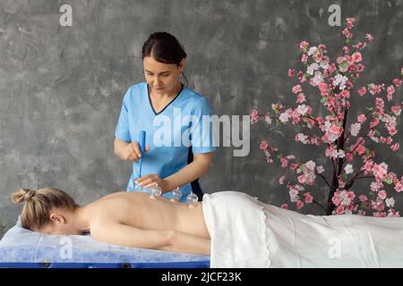 Massaggiatore in cabinet massaggiando i muscoli della schiena di una donna sdraiata sul divano con coppette da vuoto mediche. Ricevimento specializzato, massaggio professionale e. Foto Stock