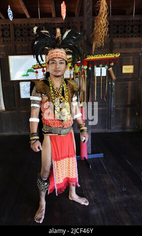 Un giovane uomo IBAN in guerriero headhunter regalia, tra cui hornbill feather headdress, al Sarawak Cultural Village vicino Kuching, Sarawak, Malesia. Foto Stock