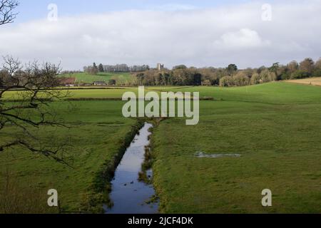 Canale di drenaggio in tipico terreno agricolo inglese con Folly in lontananza e un cielo blu e le nuvole Foto Stock