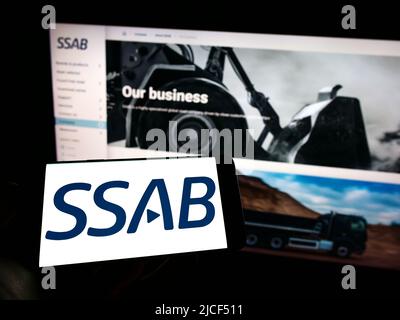 Persona che tiene il cellulare con il logo della società svedese di acciaio SSAB AB sullo schermo di fronte al sito web aziendale. Mettere a fuoco sul display del telefono. Foto Stock