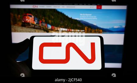 Persona che tiene uno smartphone con il logo della Canadian National Railway Company (CN) sullo schermo di fronte al sito Web. Mettere a fuoco sul display del telefono. Foto Stock