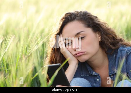 Annoiato donna che controlla smartphone seduto in un campo di grano Foto Stock