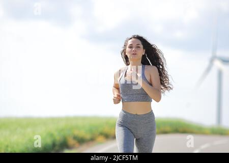 Vista frontale ritratto di una donna runner che corre in una strada in una fattoria mulino Foto Stock