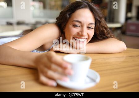 Donna felice che tiene una tazza di caffè seduta in un bar Foto Stock