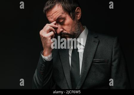 Concetto di mal di testa del proprietario di piccola impresa, uomo d'affari elegante che soffre di emicrania, ritratto a basso tasto con fuoco selettivo Foto Stock