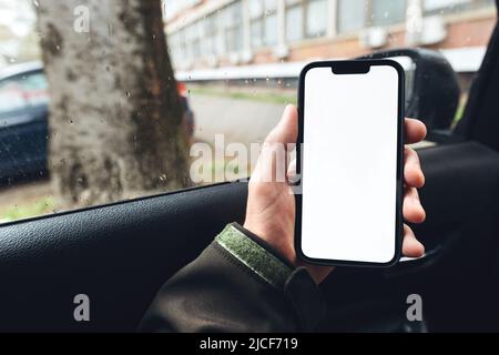 Smartphone mockup, conducente di auto che tiene il telefono cellulare con schermo bianco vuoto nel veicolo Foto Stock