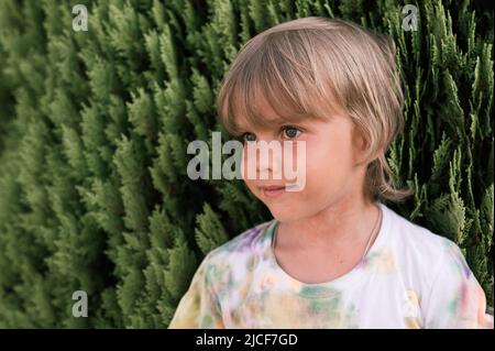 ritratto faccia di capretto felice candido ragazzo di cinque anni con problema pelle allergica e capelli biondi lunghi e occhi verdi su sfondo di pl verde Foto Stock