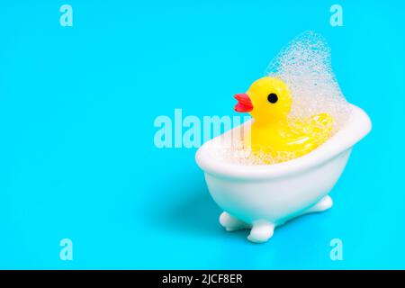 Anatra gialla in una piccola vasca bianca coperta di bolle di sapone. Concetto di bagno per bambini. Foto Stock