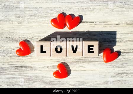 Parola AMORE disposto da blocchi di lettere di legno decorato con cuori rossi su uno sfondo di legno, vista dall'alto. Foto Stock