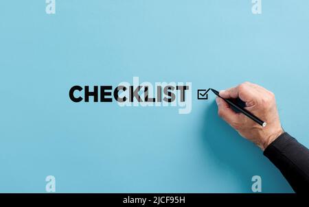 La mano maschile mette un segno di spunta accanto alla lista di controllo parola. Elenco di controllo, elenco delle attività, assegnazione di priorità o promemoria per il piano del progetto. Foto Stock