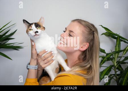 giovane donna bionda che porta il suo gatto cercando di abbracciare il gatto che non piace e cerca di scendere Foto Stock