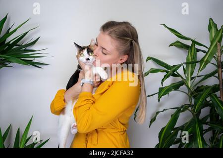 giovane donna che porta il suo gatto calico abbracciando e baciando il gattino che è dispiaciuto di esso Foto Stock