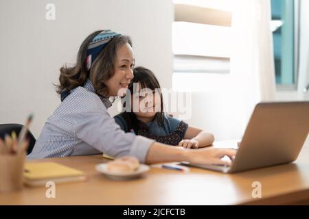 Nonna donna più anziana e nonno ragazza piccola con studio remoto di lavoro. Un'attenta e matura tutor femminile dà lezioni private alla piccola pupilla Foto Stock