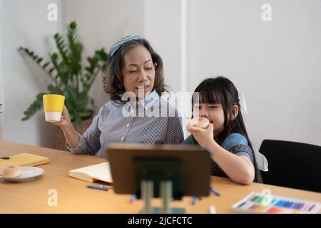 Nonna matura che aiuta a nipote con l'assegnazione della scuola, ha messo a fuoco le note di scrittura della bambina, allievo di addestramento dell'insegnante più vecchio, coinvolto in Foto Stock