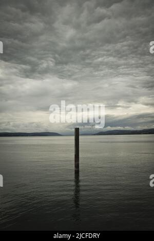 Riflesso astratto di un palo sul Lago di Costanza in una giornata nuvolosa Foto Stock