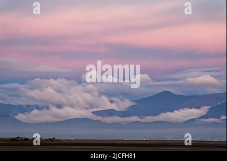 Le nuvole si depositano sulle colline dietro Nelson con il primo rosa del tramonto che colorano il cielo. Foto Stock