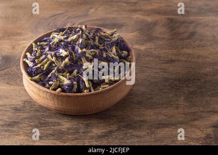 Tè blu Anchan Thai Farmer Butterfly Pea Tea. Germogli di fiori secchi organici e petali in una ciotola di legno sullo sfondo. Vite erbacea Clitoria ternatea. Foto Stock