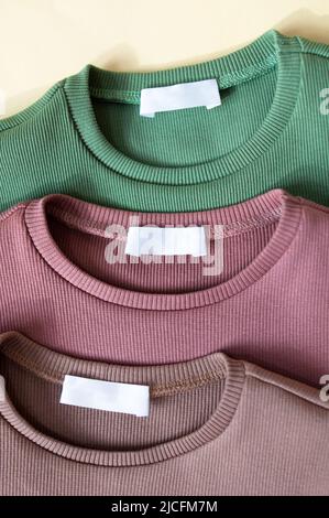 Etichette bianche di abbigliamento bianche su tre nuove camicie di cotone verde, rosa polveroso e beige tessuto tessuto fondo tessuto. Colletto tondo maniche lunghe per Foto Stock