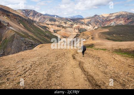 Il sentiero escursionistico di Laugavegur è il più famoso tour di trekking di più giorni in Islanda. Paesaggio girato dalla zona intorno a Landmannalaugar, punto di partenza del sentiero escursionistico a lunga distanza negli altopiani dell'Islanda. Donna (vista posteriore) con zaino a piedi il sentiero. Foto Stock