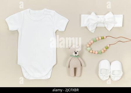 Bodysuit bianco per bebè con stivaletti e fascia per la testa. I vestiti del bambino mockup su uno sfondo beige pastello con i giocattoli dei bambini, le perle del teether e l'ac Foto Stock