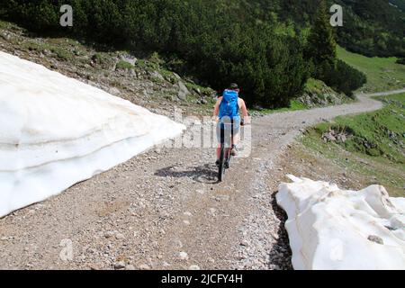 E-bike pilota giovane uomo, poco dopo la Karwendelhaus, in direzione di kleiner Ahornboden, sul lato c'è ancora la neve dell'inverno precedente Foto Stock