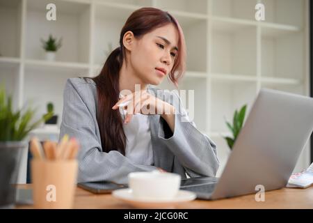 Seria giovane donna asiatica di grafica o donna d'affari in abito casual utilizzando un computer portatile, avendo un problema sul suo lavoro. Foto Stock