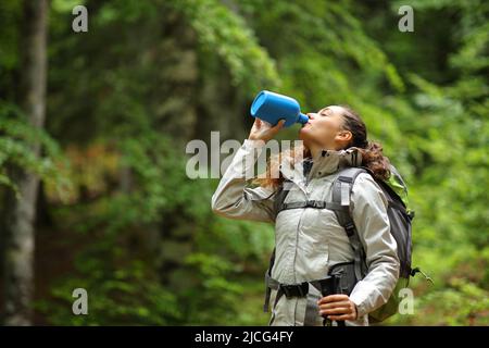 Trekker acqua potabile da mensa in piedi in una foresta verde Foto Stock