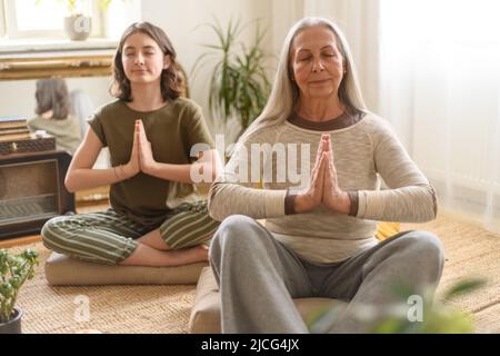 Nonna con nipote seduta sul pavimento e meditando a casa Foto Stock